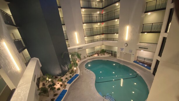 An indoor swimming pool with multiple lanes, surrounded by a poolside area with plants and a blue lounge chair. - Spacious 2-suite Condo 5-Minute Walk to the Beach. (Hilton Head Island)