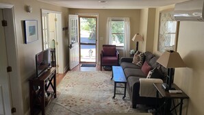 Un salon avec un canapé, une table basse, un téléviseur et une lampe. Une porte donne sur un balcon.
