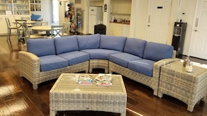 Ein Wohnzimmer mit einem blauen Modulsessel, einem Korbtisch und einem Essbereich mit Tisch und Stühlen.