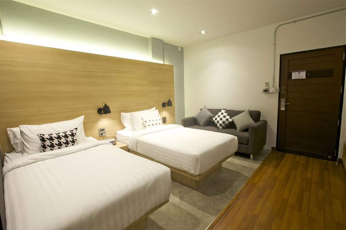 Quarto de hotel com duas camas, um sofá, uma cabeceira de madeira e uma porta.