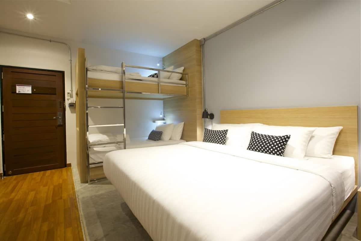 Quarto de hotel com beliche, porta de madeira e cama com roupa de cama branca e almofadas preto e branco.