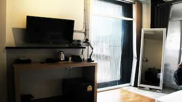 A hotel room with a television on a wooden desk, a mirror, and a window with blinds.