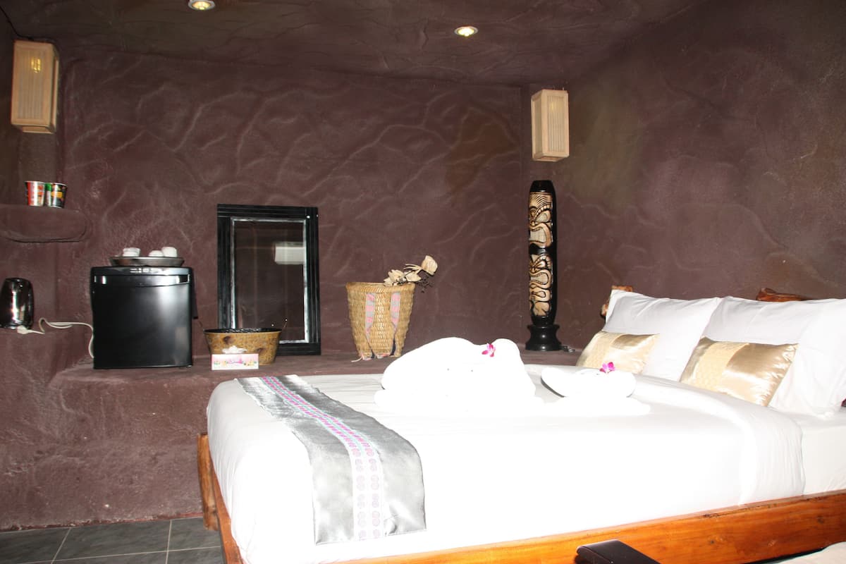A bedroom with a bed, a trash bin, a basket, and a tall decorative item.