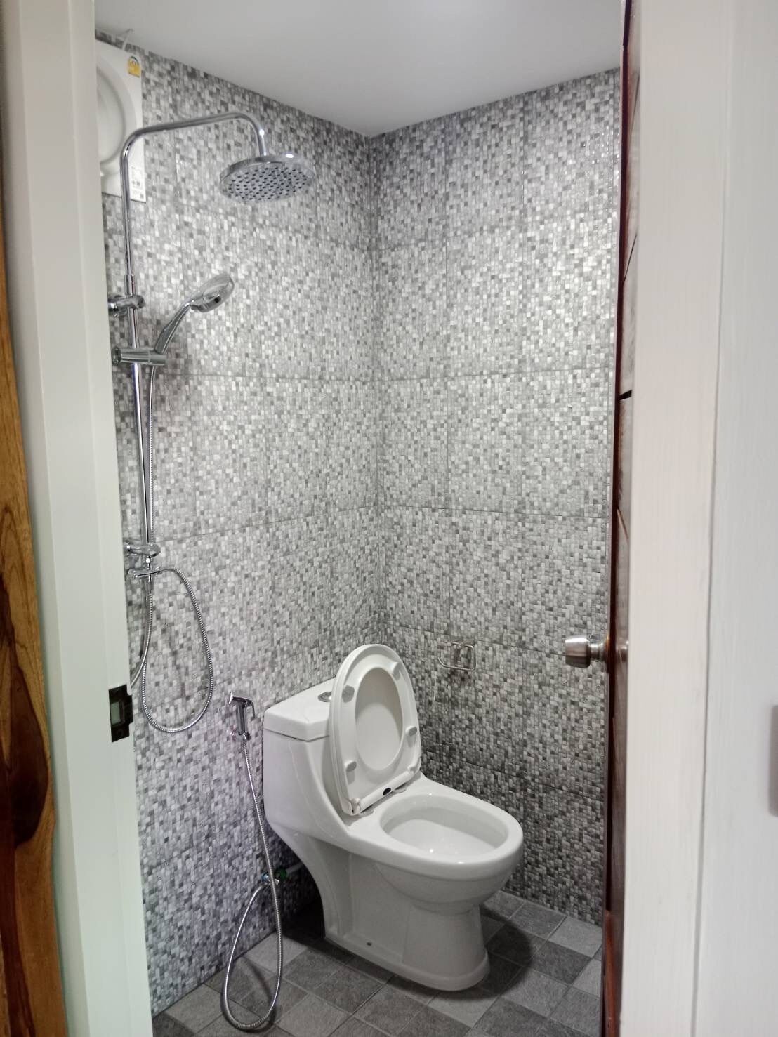 A bathroom with a toilet, a shower, and a tiled wall.