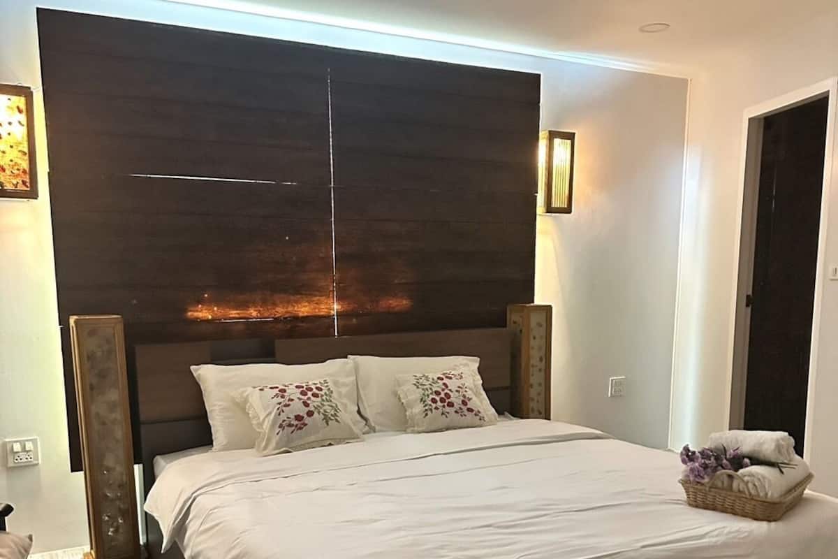 A modern bedroom with a large bed, dark headboard, and ambient lighting.
