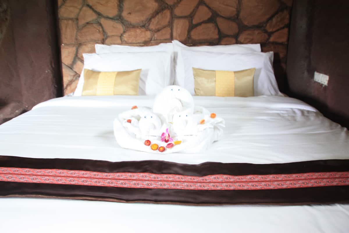 A neatly made bed with white linens, two pillows, and a decorative arrangement of towels and fruits.