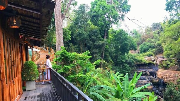 A wooden deck with a railing overlooking a lush garden and a small waterfall. - Sainamtok Resort (Khao Kho)