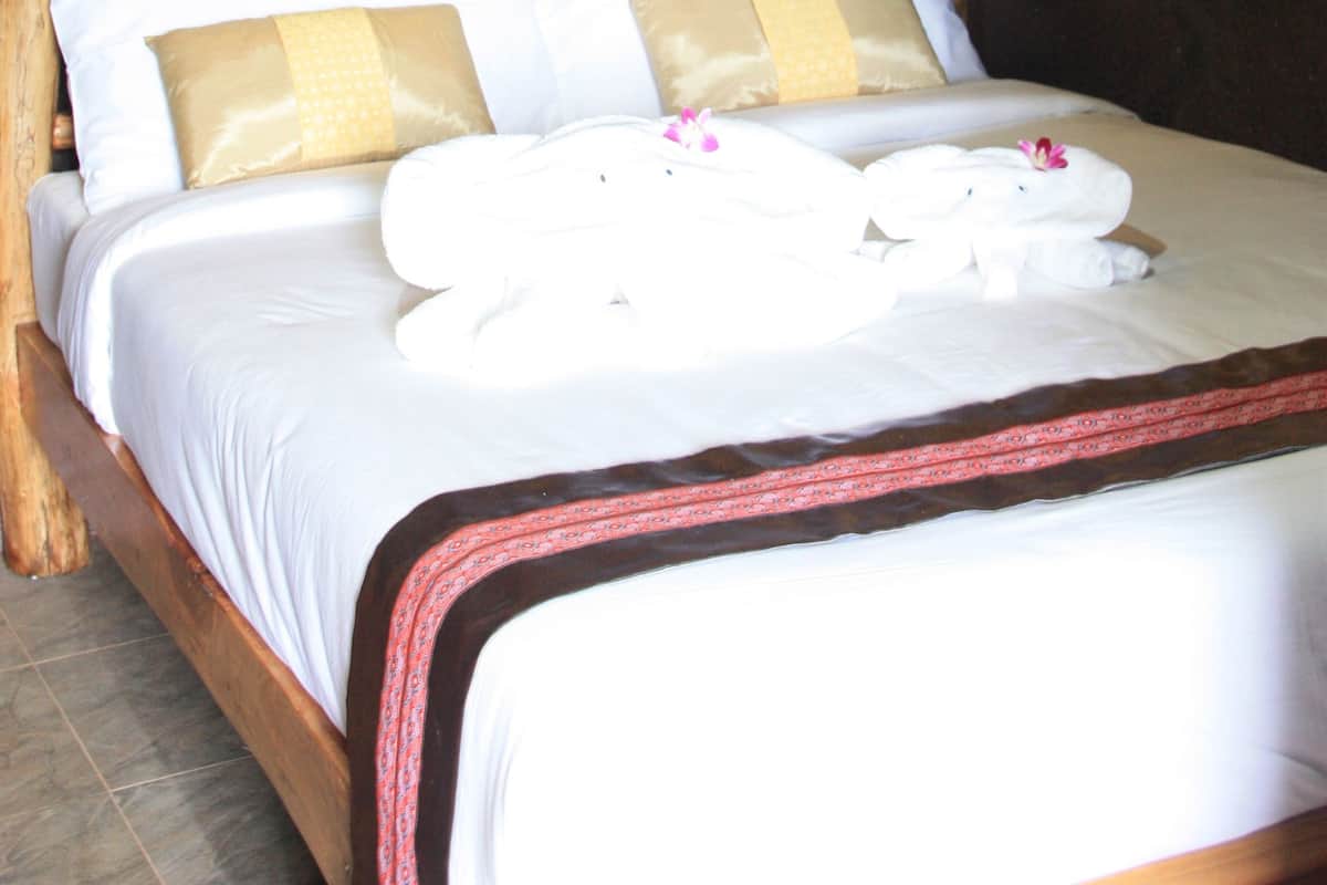 A neatly made bed with white linens and decorative pillows, a woven basket, and a tall decorative item on a shelf above the bed.