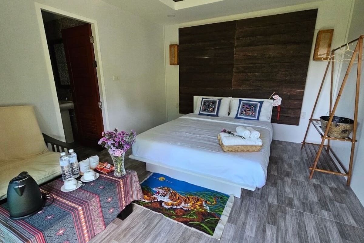 A bedroom with a bed, bedside table, and a small table with a vase and towels.
