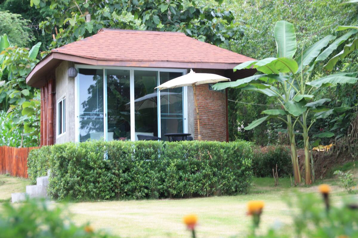 A small house with a red roof, large windows, and a patio umbrella.