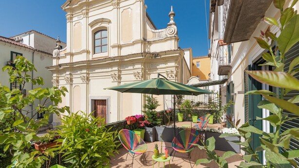 Un patio con una iglesia, mesas al aire libre y plantas en macetas.