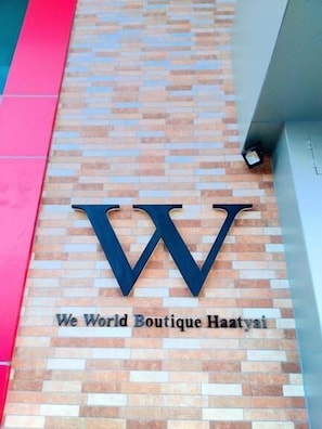A sign with the logo and name "We World Boutique Haayai" on a brick wall.