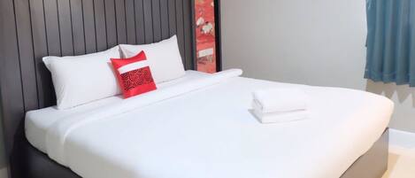 A neatly made bed with white bedding and a red pillow, a dark headboard, and a red decorative panel on the wall.