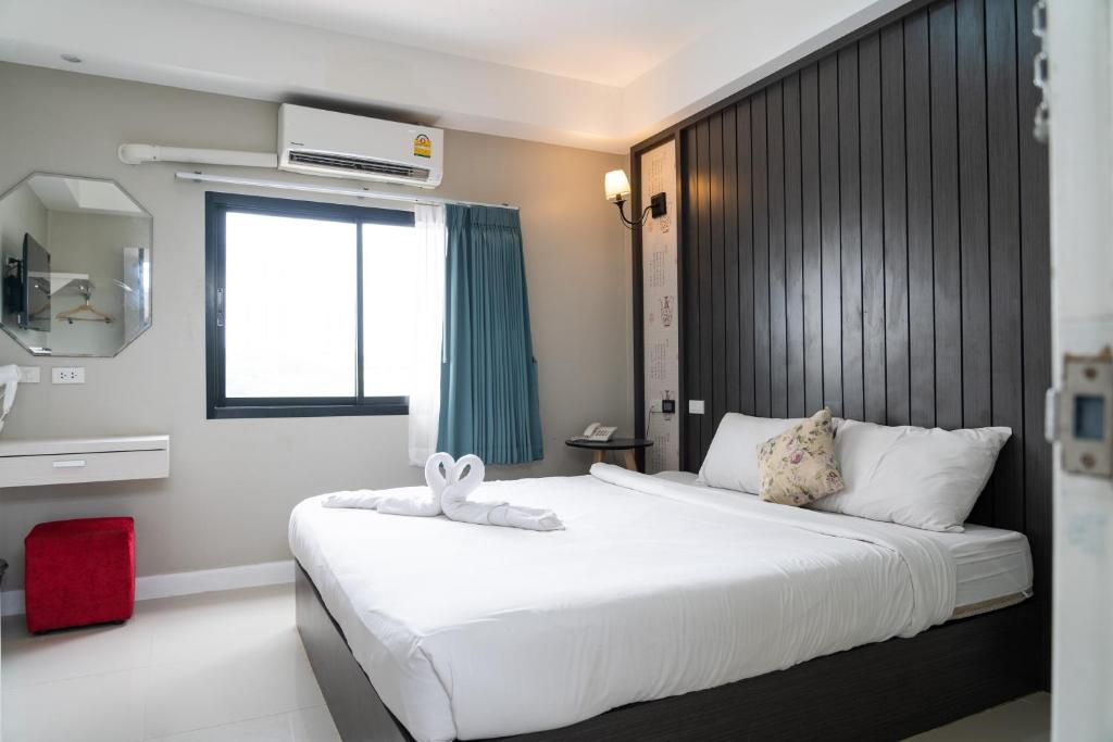A hotel room with a bed, a bedside table, a mirror, an air conditioning unit, and a window with curtains.