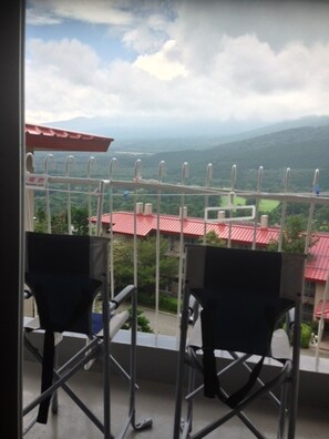 A balcony with two chairs and a metal railing, overlooking a landscape with red-roofed buildings and green hills. - Fuji Subashiri Condominium Tannpopo (Oyama)