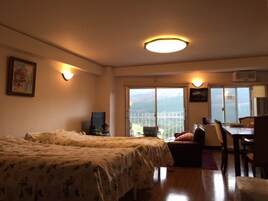 A hotel room with two beds, a desk, and a chair. There is a large window with a view of mountains.