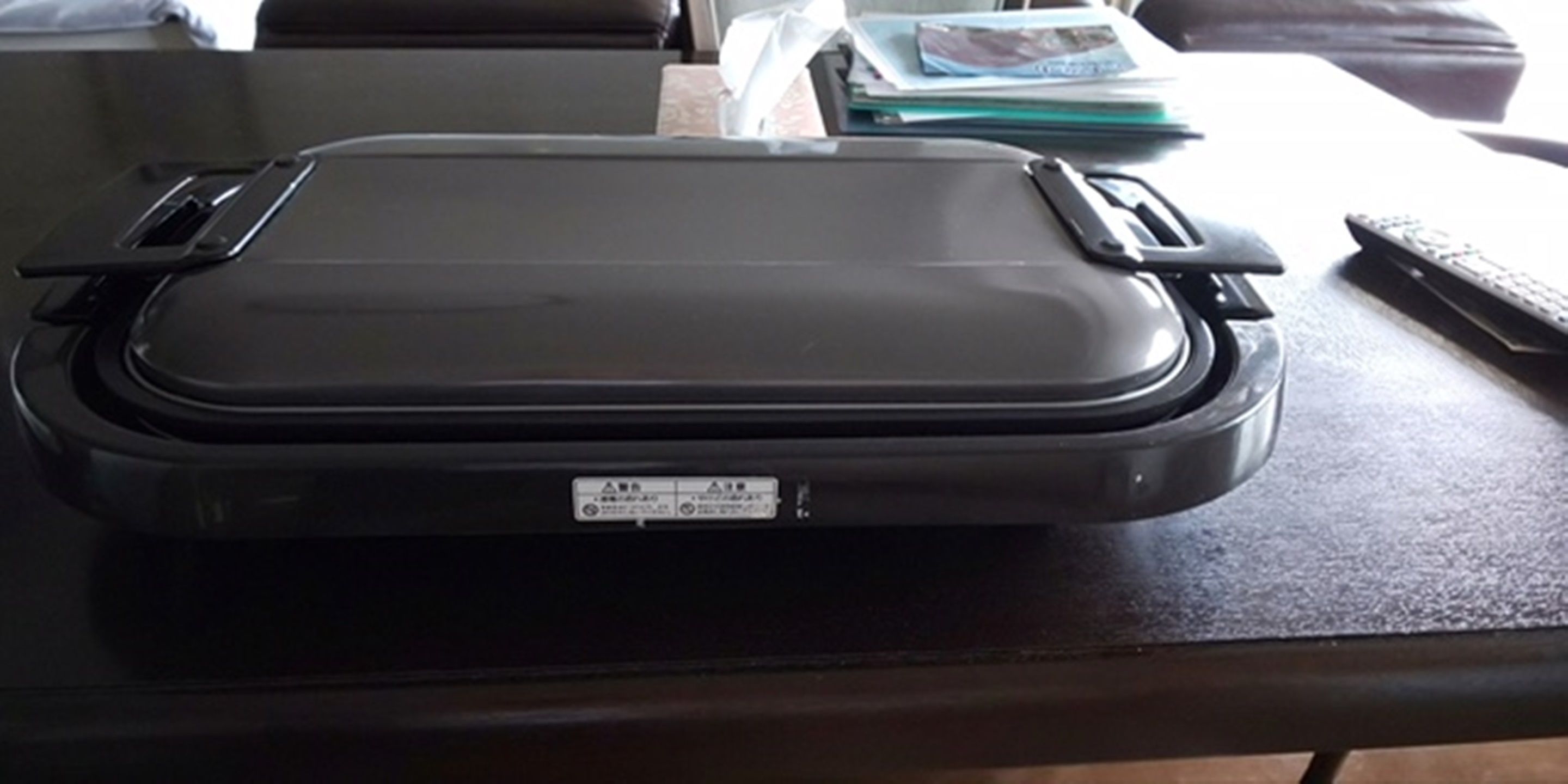 A black suitcase on a table with a remote control and some papers nearby.