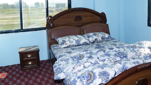 A bedroom with a wooden bed, floral bedding, a small bedside table, and a window with a view of fields. - Lincoln Holiday Home (Tohka)