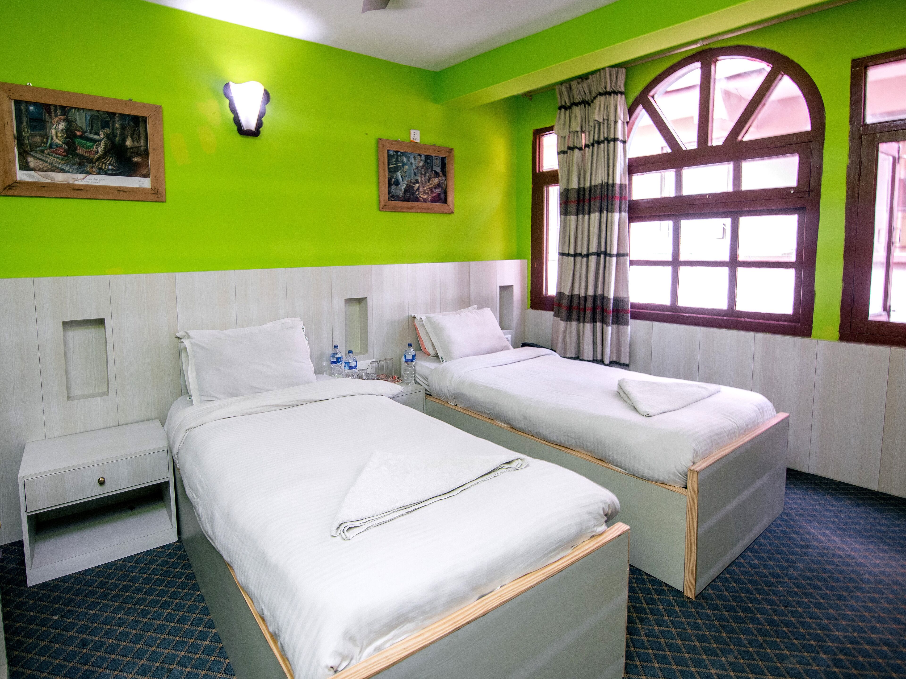 Habitación de hotel con dos camas, un ventanal con cortinas y obras de arte en las paredes.