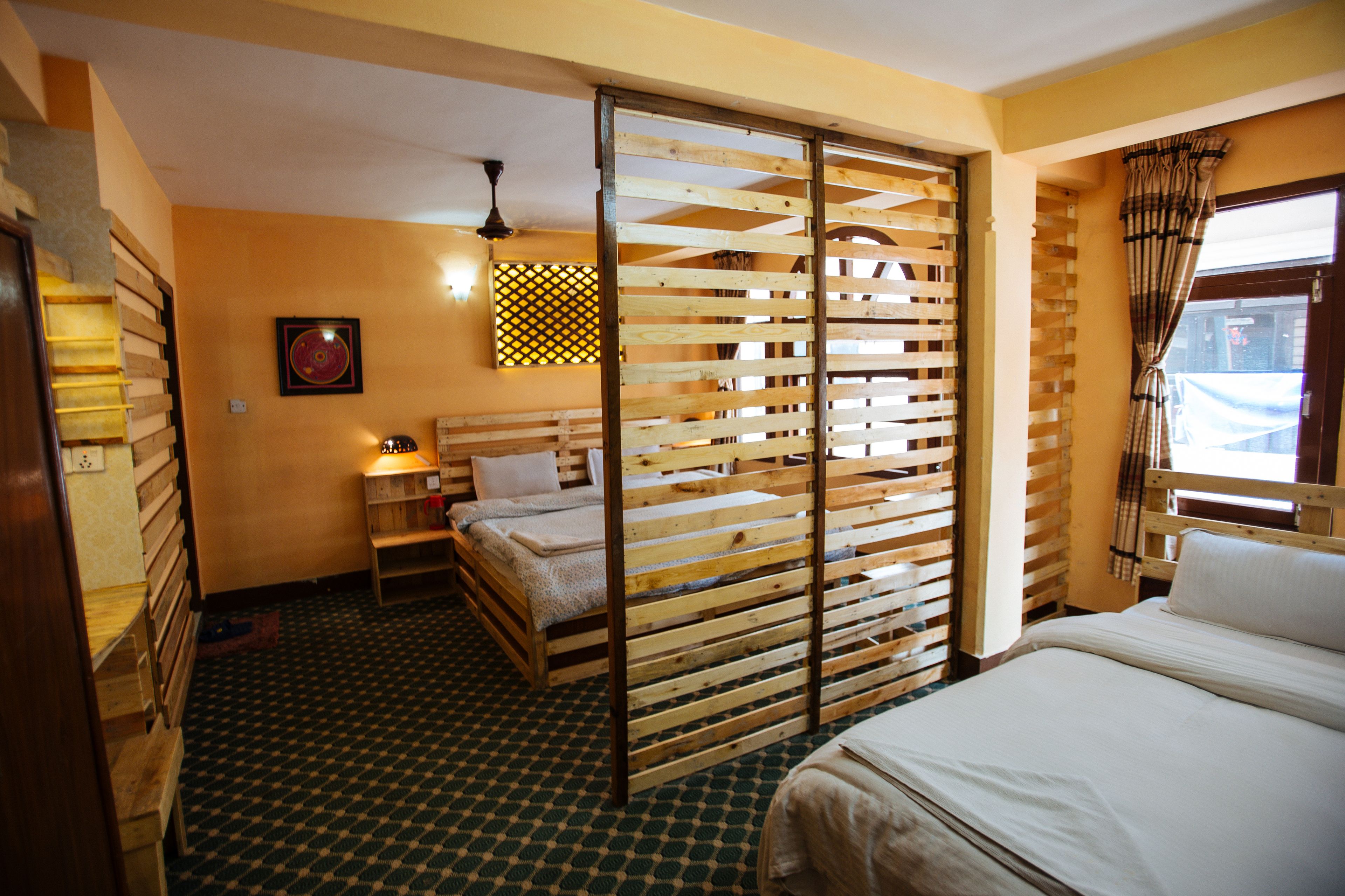 A room with a bed, a wooden partition, a small table with a lamp, and a patterned floor.