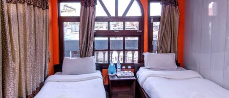 A hotel room with two beds, a window with a view, and a small table with a water bottle and glasses.