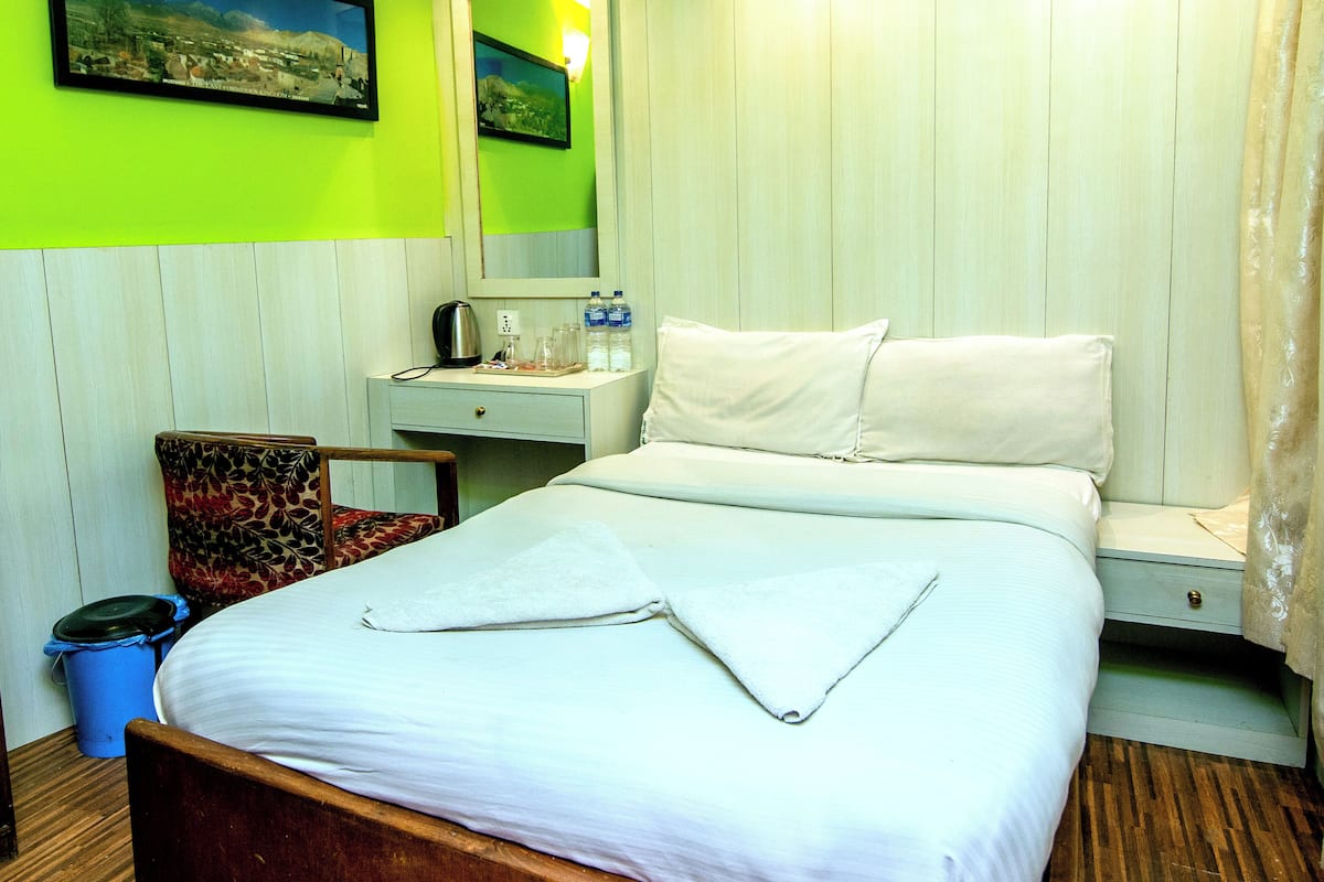 Une chambre d’hôtel avec un lit, un bureau, une chaise, une poubelle et un miroir.