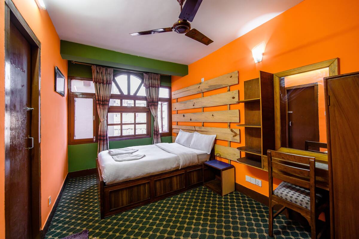 Une chambre avec un lit, un ventilateur de plafond, une fenêtre avec des rideaux et une tête de lit en bois.