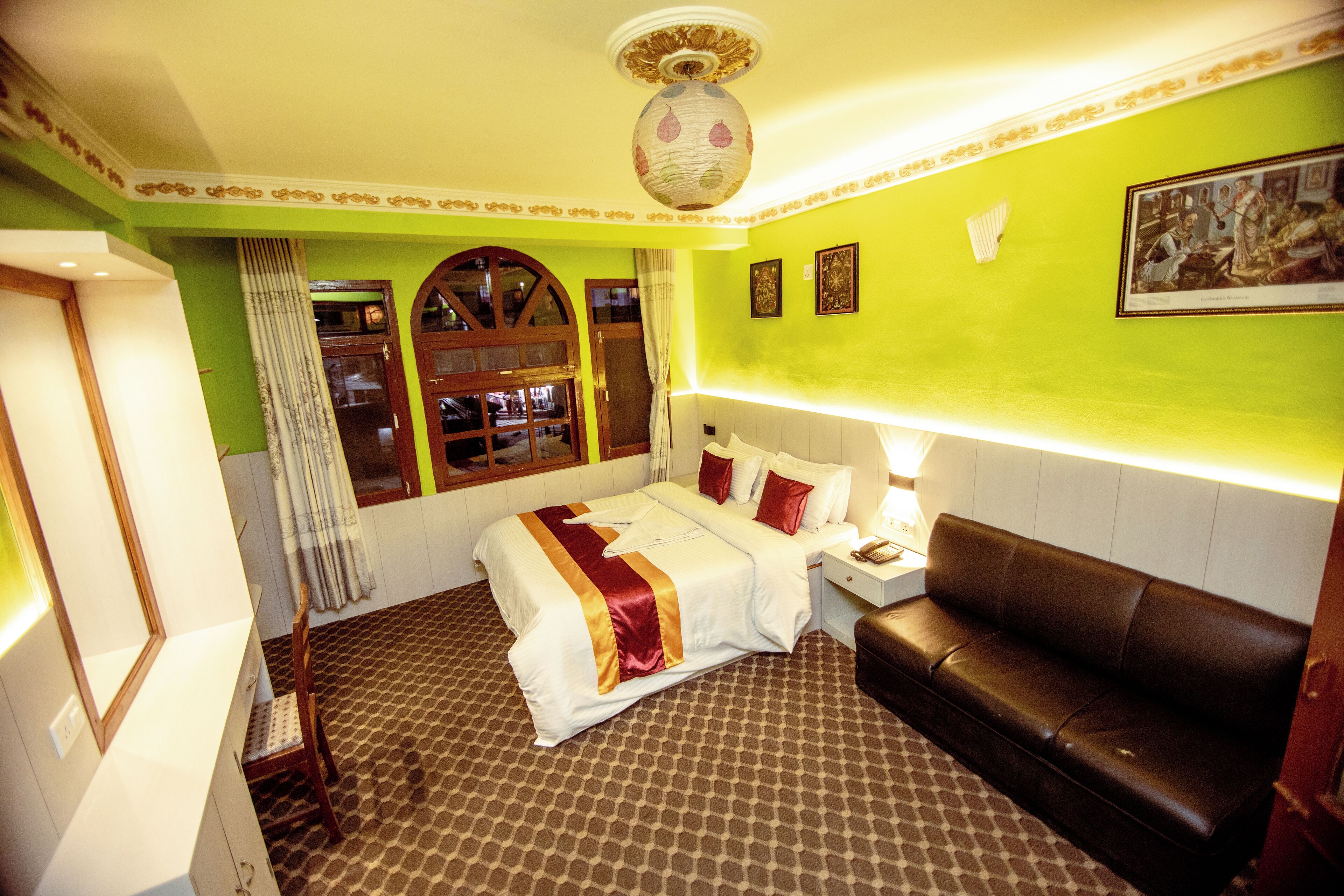 Une chambre d’hôtel avec un lit, un canapé, une table de chevet, un miroir et une fenêtre avec des rideaux.