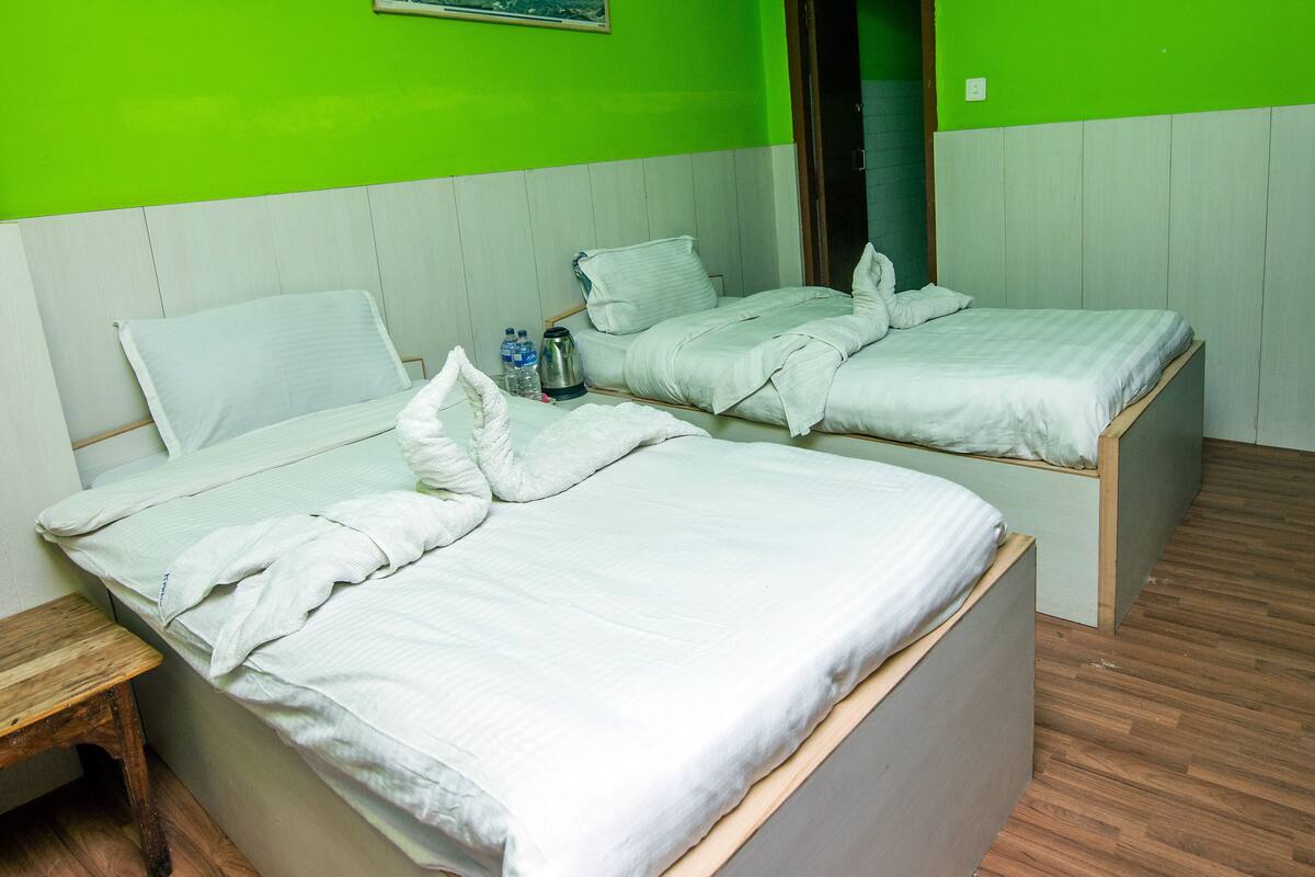 Une chambre avec deux lits, un banc en bois et un mur vert orné d’une image de montagne.