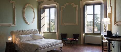 A bedroom with a large bed, two chairs, a table, and a window.