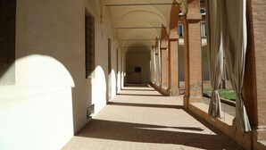 A corridor with arches, a tiled floor, and a window with curtains. - Antico Convento San Francesco (Bagnacavallo)