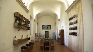 A dining area with a long table, chairs, and a wall with bottles. There are shelves with plants and decorative items on the left. - Antico Convento San Francesco (Bagnacavallo)