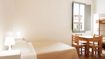 Ein Hotelzimmer mit einem Bett, einem Nachttisch mit Lampe, einem Holztisch mit Stühlen und einem Fenster mit Blick auf Gebäude.