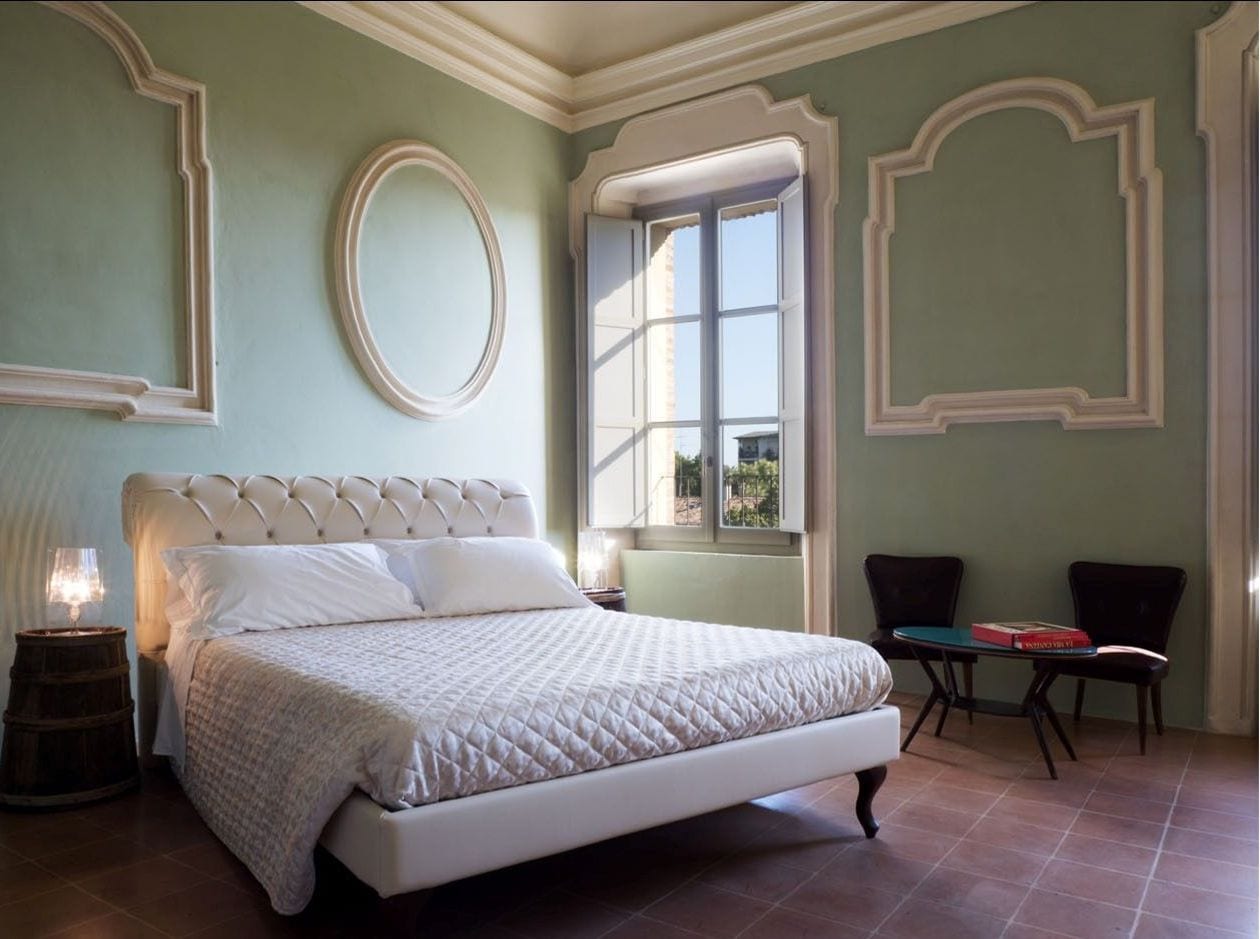 A bedroom with a large bed, a window with curtains, a table, and two chairs.