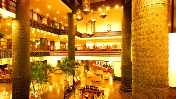 A multi-level hotel lobby with a central open space, multiple seating areas, and decorative columns with inscriptions. - International Asia-Pacific Convention Center (Sanya)