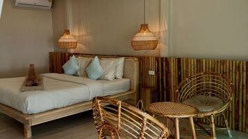 Een kamer met een bed, twee rieten stoelen, een klein rond tafeltje en twee hangende rieten lampen.