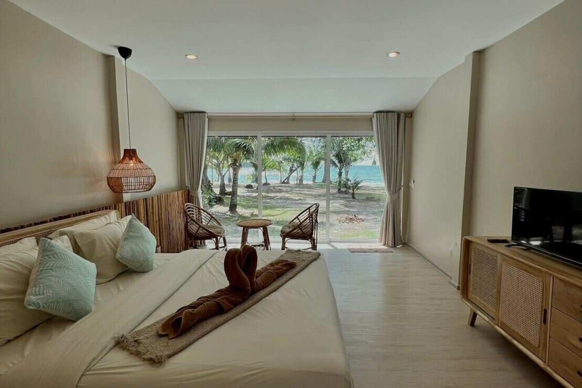 A spacious bedroom with a large bed, a TV, and a view of the beach.