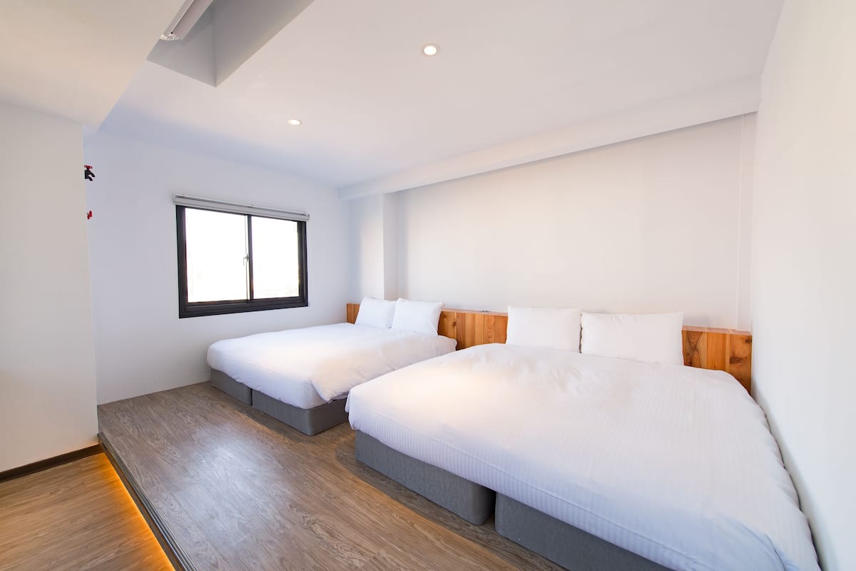 Une chambre d’hôtel avec deux lits, une grande fenêtre et un plancher en bois.