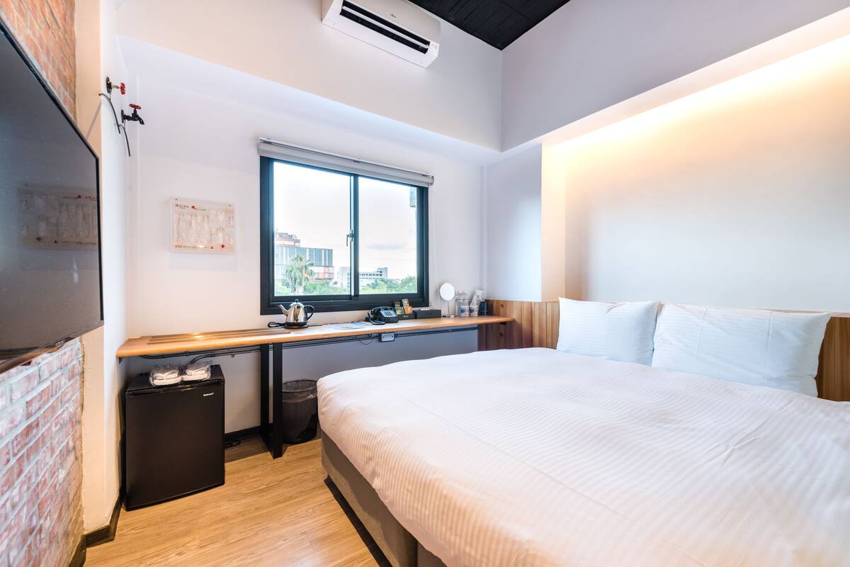 Une chambre avec un lit, un bureau, une fenêtre et un petit réfrigérateur.