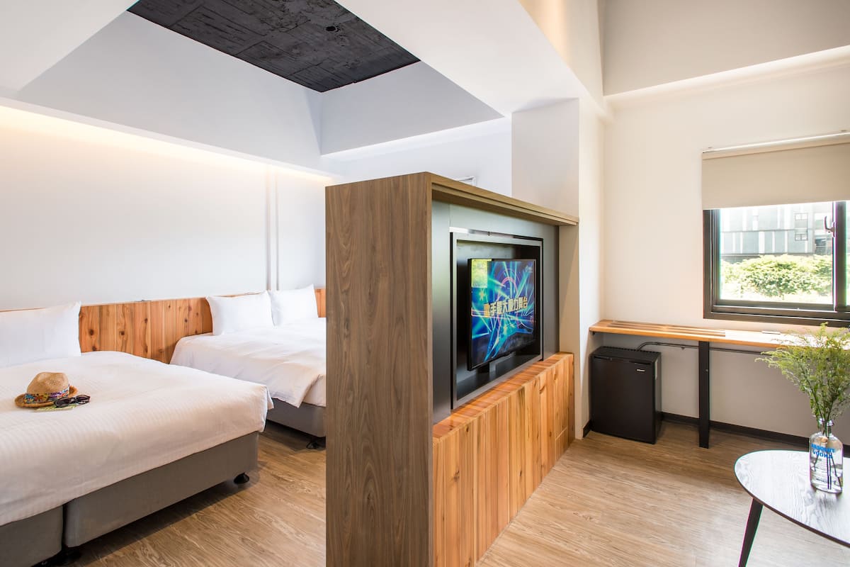 Une chambre d’hôtel avec deux lits, une télévision, une petite table et une fenêtre donnant sur un paysage verdoyant.