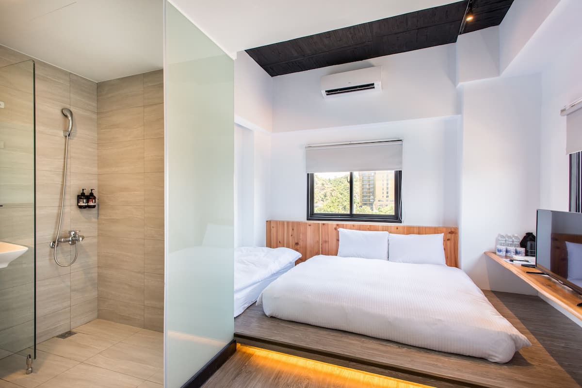 Une chambre d’hôtel moderne équipée d’une douche, d’un lit, d’une télévision et d’une fenêtre donnant sur un paysage agréable.