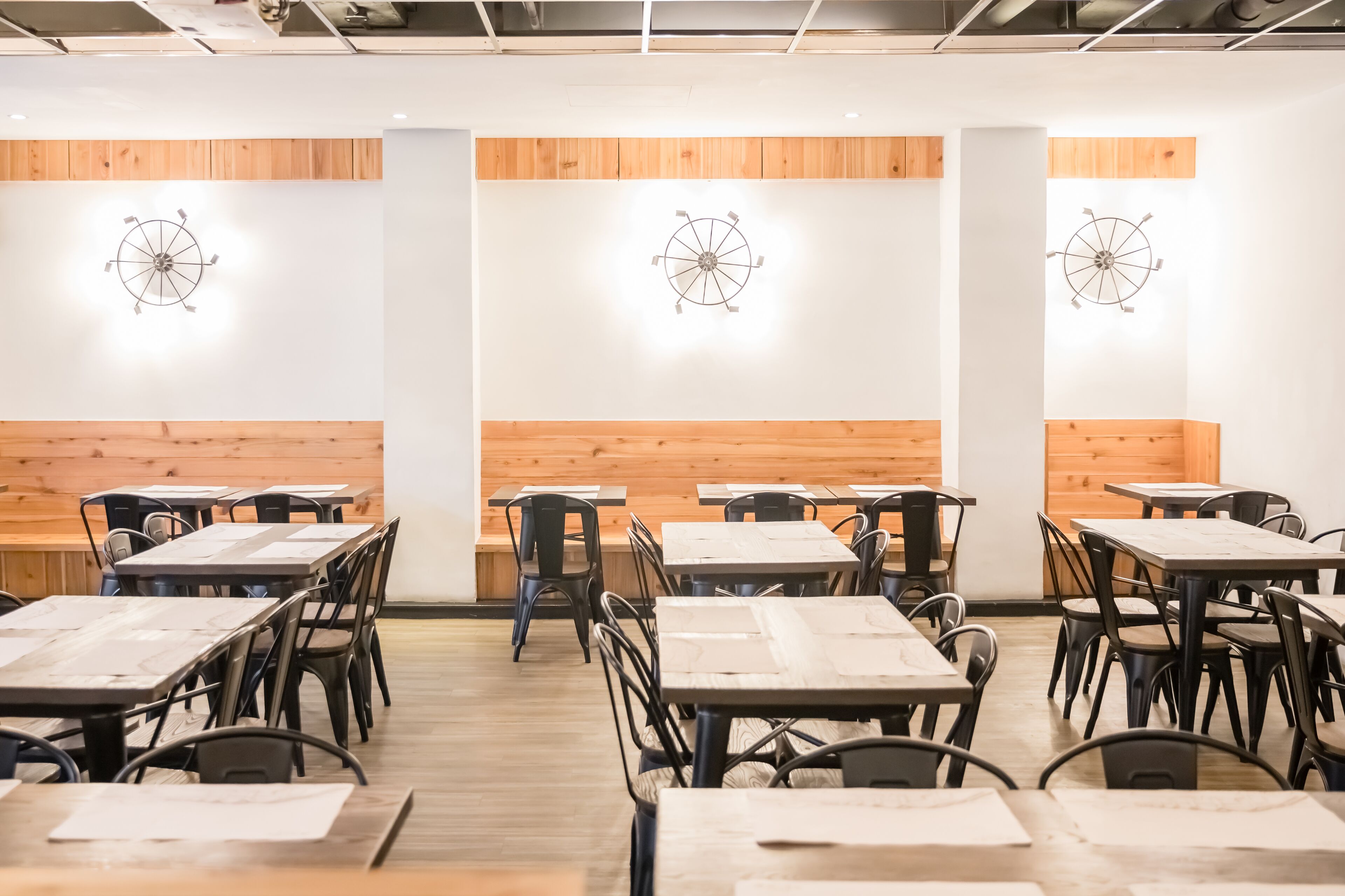 A restaurant interior with wooden panel walls, round ceiling light fixtures, and black metal chairs and tables.