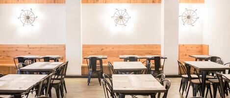 A restaurant interior with wooden panel walls, round ceiling light fixtures, and black metal chairs and tables.