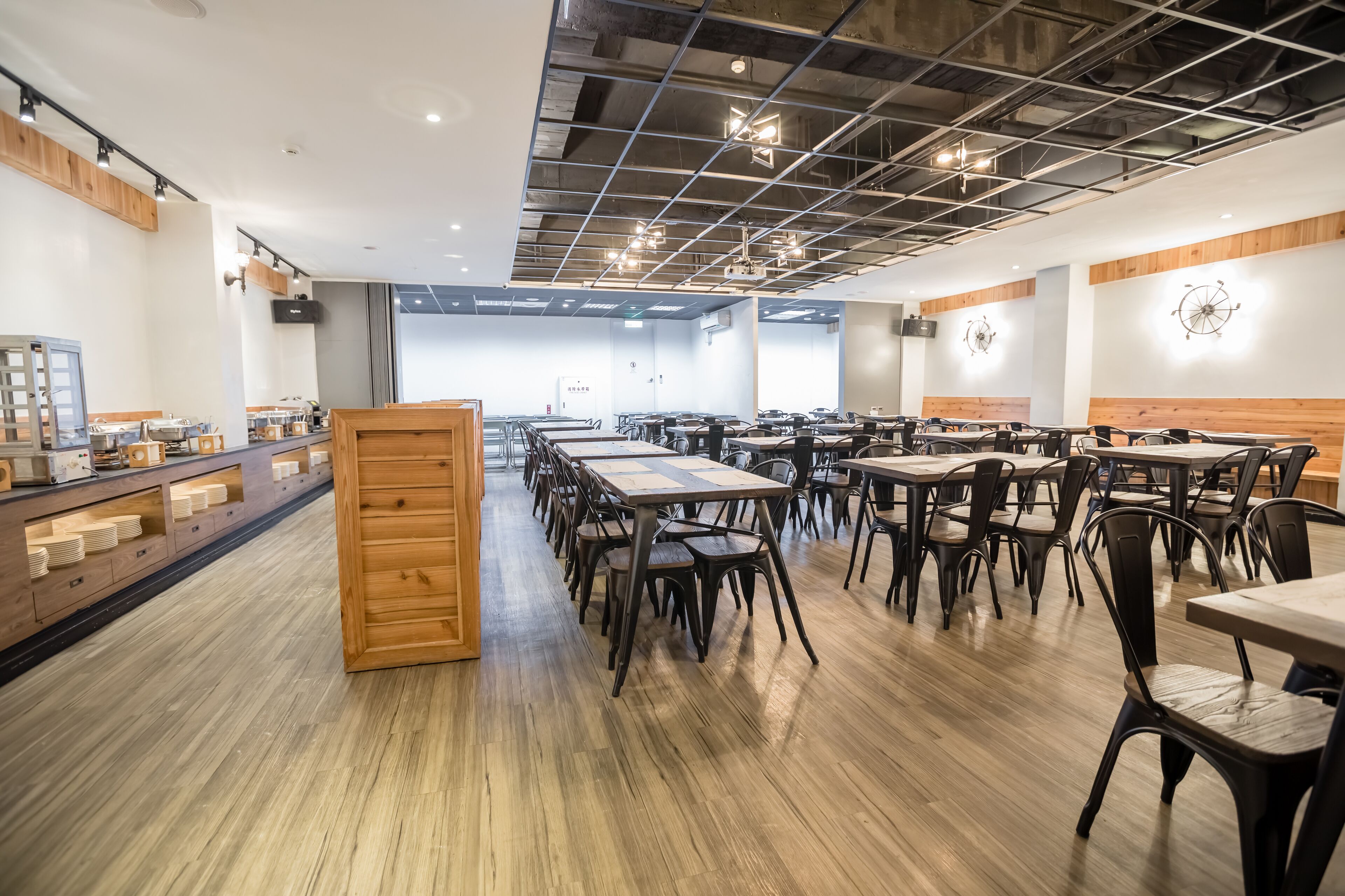 A spacious dining area with multiple tables and chairs, wooden flooring, and a modern ceiling design.