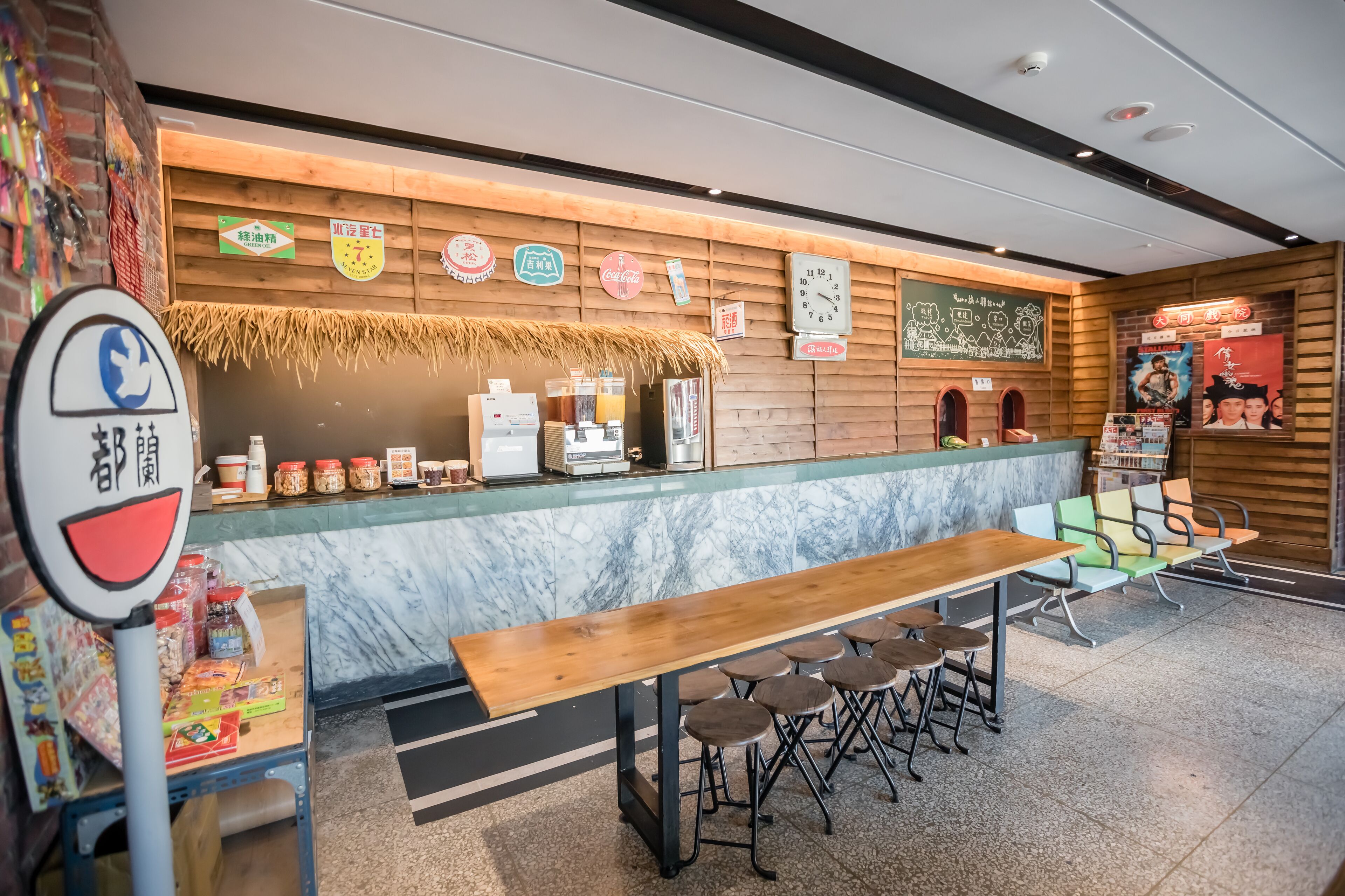 A cafe with a wooden counter, stools, and a variety of food items displayed.