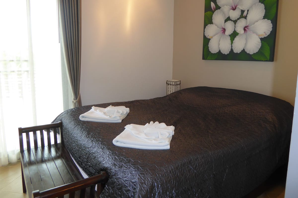A hotel room with a large bed, a wooden chair, and a painting of white flowers on the wall.