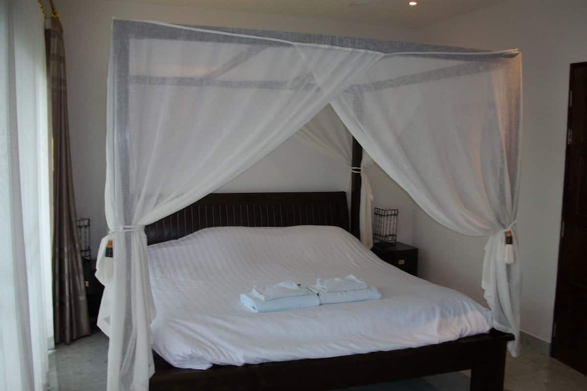 A four-poster bed with white linens and a canopy.