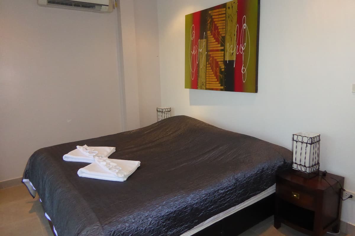 A bedroom with a bed, a nightstand, and a wall-mounted air conditioner.