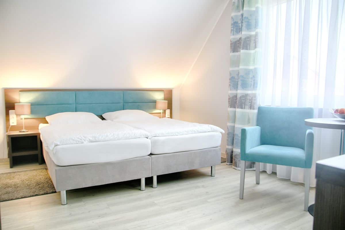 Een moderne hotelkamer met een tweepersoonsbed, nachtkastjes met lampen, een lichtblauwe fauteuil en een kleine ronde tafel.