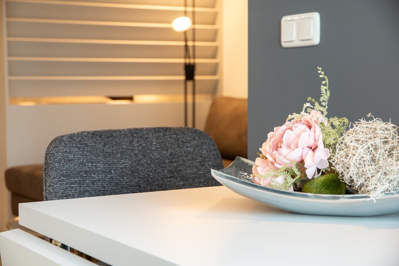 A modern room with a grey sofa, a white table, and a decorative plant arrangement.